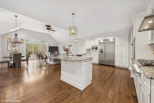 kitchen featuring pendant lighting, white cabinets, ceiling fan with notable chandelier, a center island with sink, and built in appliances