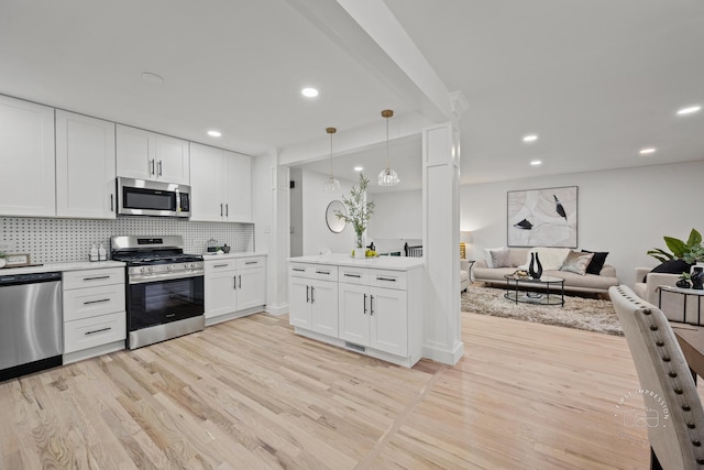 kitchen featuring light wood-type flooring, tasteful backsplash, stainless steel appliances, decorative light fixtures, and white cabinetry