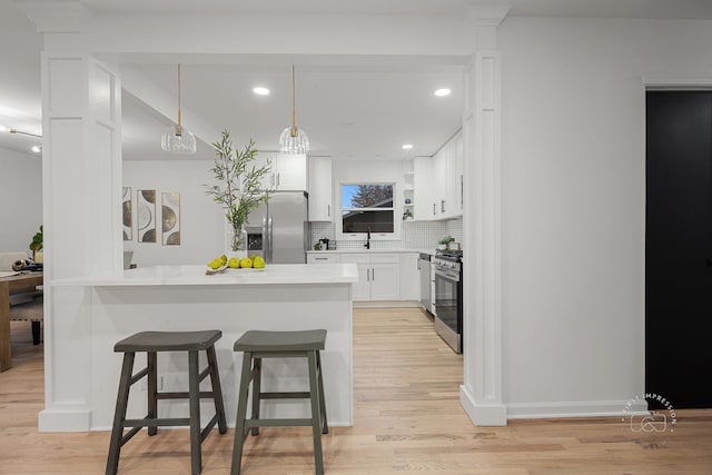 kitchen featuring a kitchen bar, tasteful backsplash, stainless steel appliances, light hardwood / wood-style flooring, and white cabinetry