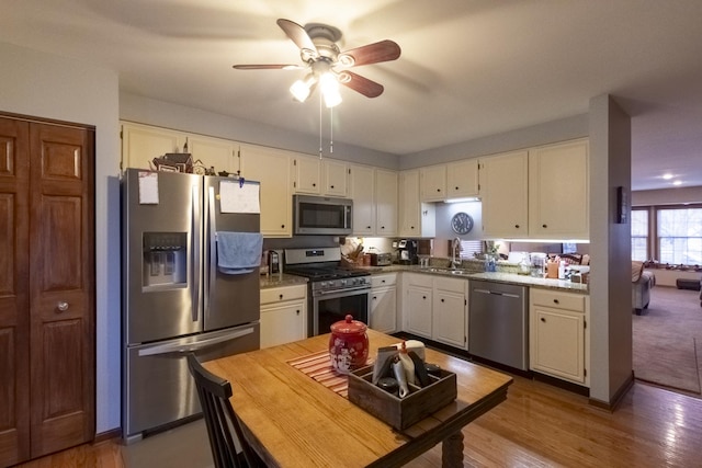 kitchen featuring appliances with stainless steel finishes, light stone counters, sink, hardwood / wood-style flooring, and white cabinets