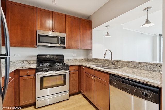 kitchen with sink, light stone counters, light hardwood / wood-style floors, hanging light fixtures, and appliances with stainless steel finishes