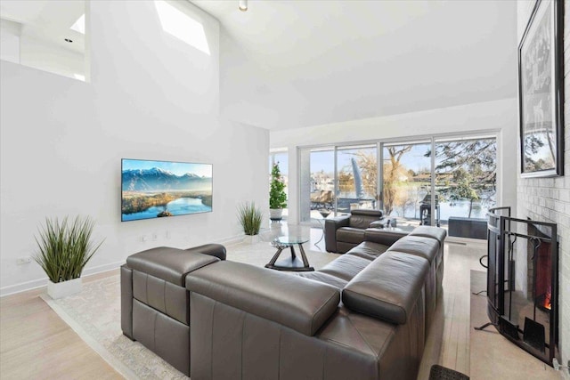 living room with light wood-type flooring, a high ceiling, and a brick fireplace