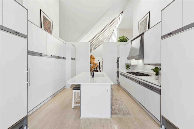 kitchen with a breakfast bar, custom range hood, white cabinetry, and an island with sink