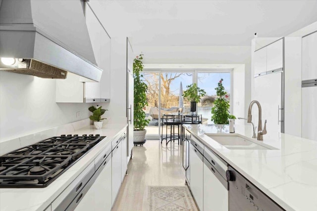 kitchen featuring white cabinetry, sink, light stone countertops, wall chimney range hood, and gas stovetop