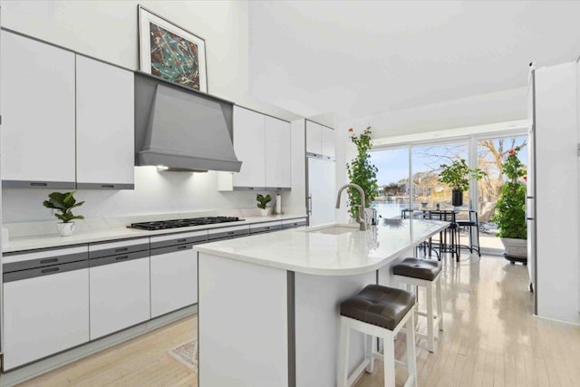 kitchen with stainless steel gas stovetop, a breakfast bar, a kitchen island with sink, sink, and custom range hood