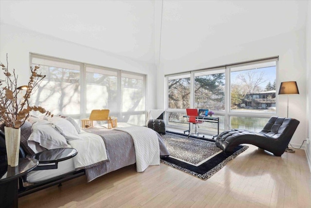 bedroom featuring multiple windows, a high ceiling, and light wood-type flooring