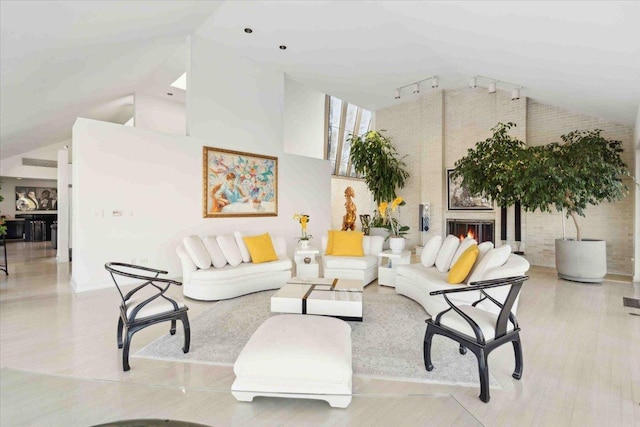 living room with brick wall, a fireplace, high vaulted ceiling, and track lighting