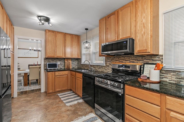 kitchen with sink, an inviting chandelier, dark stone countertops, pendant lighting, and appliances with stainless steel finishes