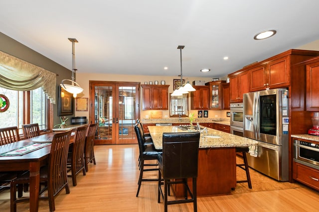 kitchen with appliances with stainless steel finishes, light wood-type flooring, french doors, light stone counters, and hanging light fixtures