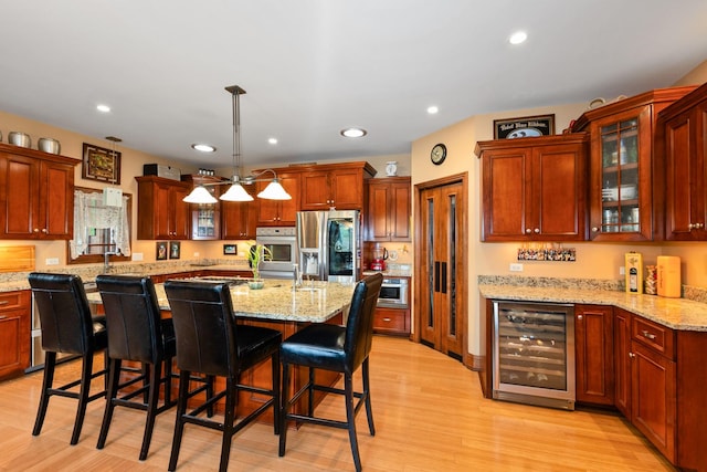 kitchen featuring stainless steel appliances, wine cooler, pendant lighting, light hardwood / wood-style floors, and a breakfast bar