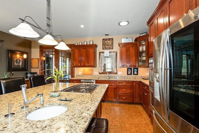 kitchen featuring light stone countertops, sink, stainless steel appliances, decorative light fixtures, and a kitchen bar