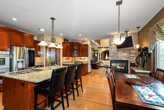 kitchen featuring a fireplace, light wood-type flooring, hanging light fixtures, and stainless steel appliances