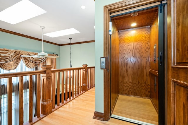 hallway with a skylight, elevator, crown molding, and light hardwood / wood-style floors