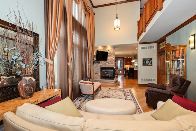 living room with light hardwood / wood-style floors, a stone fireplace, crown molding, and a high ceiling