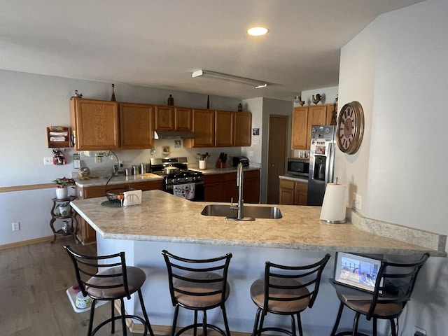 kitchen featuring kitchen peninsula, a kitchen bar, stainless steel appliances, dark wood-type flooring, and sink