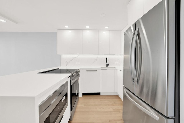 kitchen with appliances with stainless steel finishes, tasteful backsplash, sink, white cabinets, and light hardwood / wood-style floors