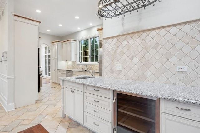 kitchen featuring light stone countertops, backsplash, wine cooler, and sink