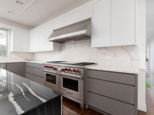 kitchen with range with two ovens, wall chimney range hood, gray cabinets, light stone countertops, and white cabinetry