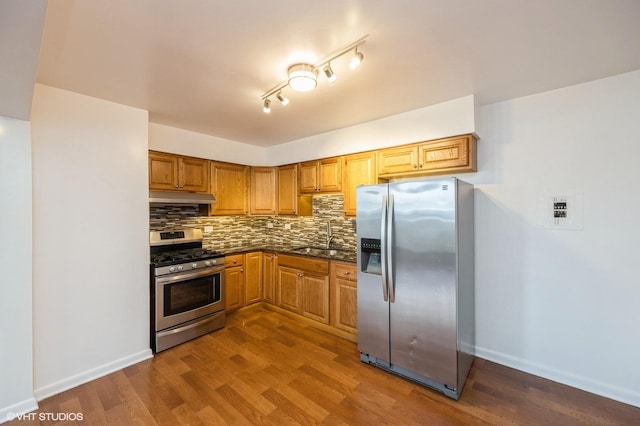 kitchen with hardwood / wood-style floors, dark stone countertops, appliances with stainless steel finishes, decorative backsplash, and sink