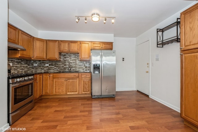 kitchen featuring stainless steel appliances, exhaust hood, tasteful backsplash, dark hardwood / wood-style flooring, and sink