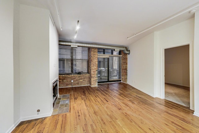 unfurnished living room with hardwood / wood-style floors and brick wall