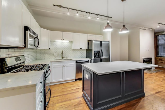 kitchen with white cabinetry, sink, decorative light fixtures, a kitchen island, and appliances with stainless steel finishes