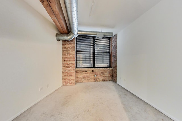 carpeted empty room featuring brick wall