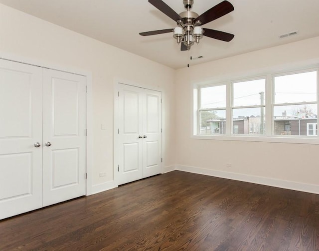 unfurnished bedroom featuring ceiling fan, dark hardwood / wood-style flooring, and two closets