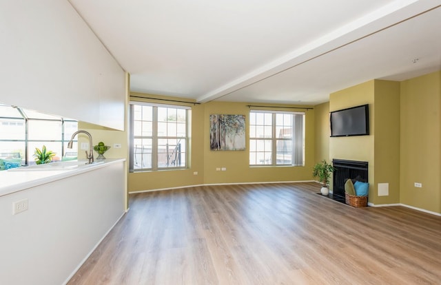 unfurnished living room featuring beamed ceiling and light wood-type flooring