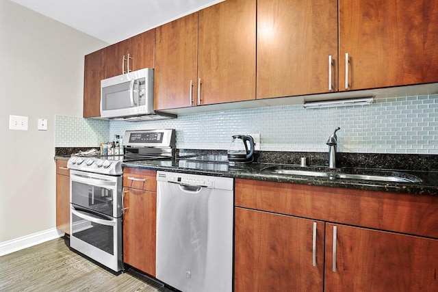 kitchen with sink, backsplash, light hardwood / wood-style floors, dark stone counters, and appliances with stainless steel finishes