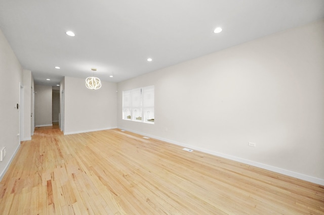 spare room featuring a notable chandelier and light hardwood / wood-style floors