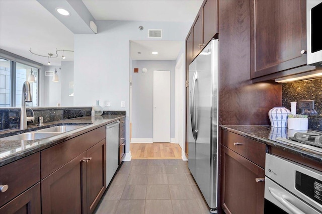 kitchen with appliances with stainless steel finishes, tasteful backsplash, dark stone counters, sink, and hanging light fixtures