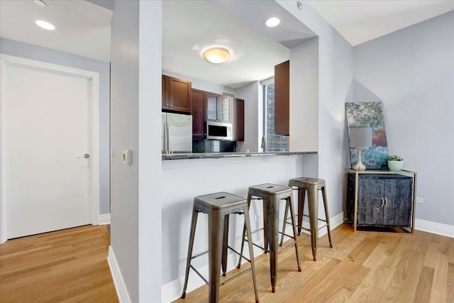 kitchen with kitchen peninsula, a kitchen breakfast bar, light wood-type flooring, dark stone counters, and fridge