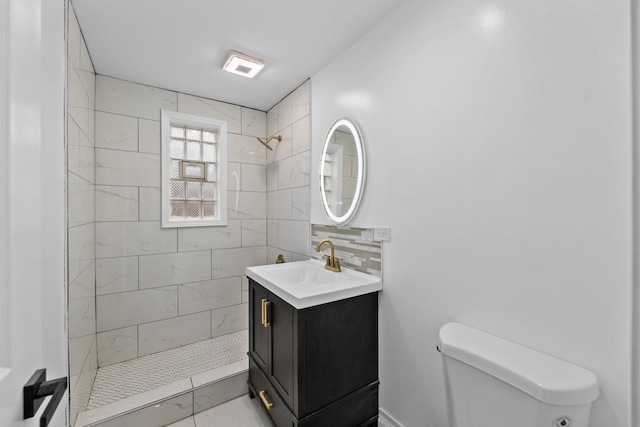 bathroom with vanity, tile patterned flooring, toilet, tasteful backsplash, and a tile shower