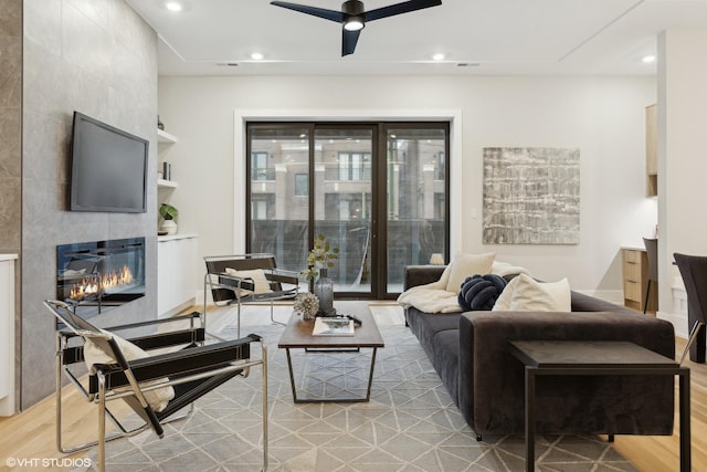 living room featuring a tiled fireplace, ceiling fan, and light hardwood / wood-style flooring