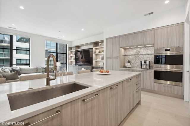 kitchen with light stone countertops, light brown cabinetry, double oven, and sink