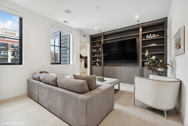 living room featuring built in shelves, light wood-type flooring, and plenty of natural light