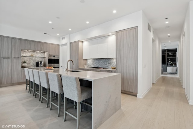 kitchen featuring backsplash, sink, an island with sink, a breakfast bar area, and stainless steel gas cooktop