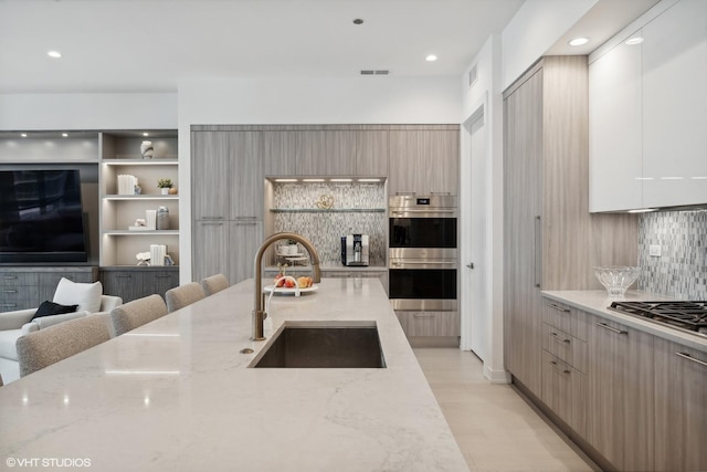 kitchen with sink, stainless steel appliances, a kitchen breakfast bar, tasteful backsplash, and light stone counters