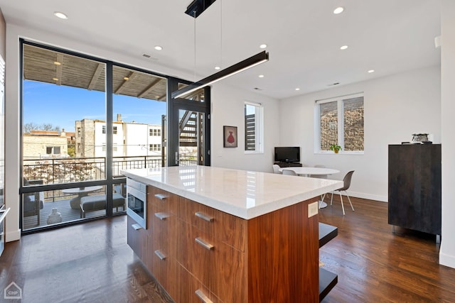 kitchen featuring dark hardwood / wood-style flooring, a center island, decorative light fixtures, and stainless steel microwave