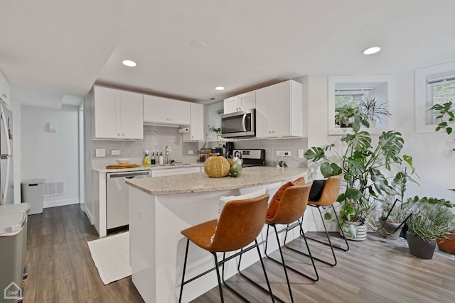 kitchen with white cabinetry, sink, stainless steel appliances, hardwood / wood-style floors, and a kitchen bar