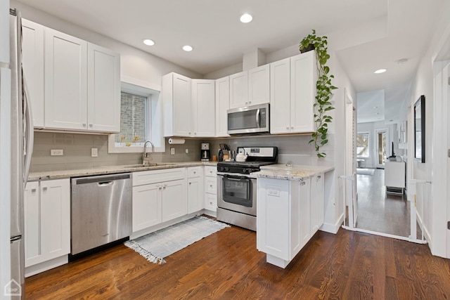 kitchen with light stone counters, stainless steel appliances, dark wood-type flooring, sink, and white cabinetry