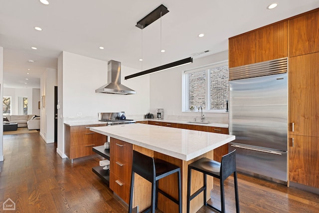 kitchen featuring a kitchen bar, wall chimney exhaust hood, stainless steel built in refrigerator, sink, and a center island