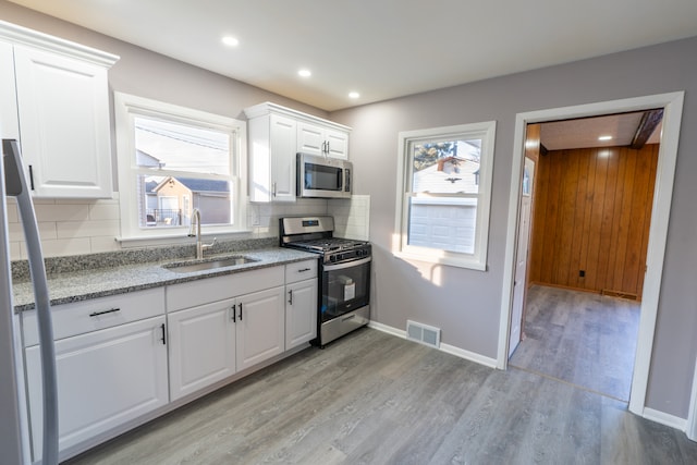 kitchen with stainless steel appliances, white cabinetry, sink, and backsplash