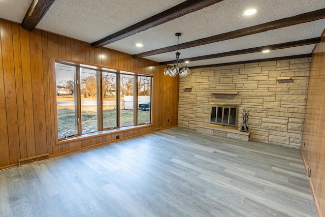 unfurnished living room featuring beam ceiling, wooden walls, and a stone fireplace