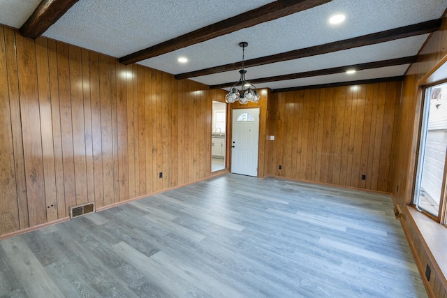 empty room featuring a textured ceiling, wooden walls, a notable chandelier, hardwood / wood-style flooring, and beam ceiling