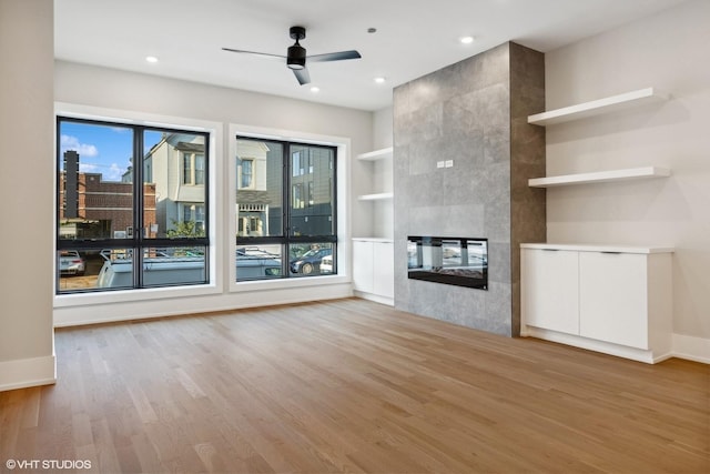 unfurnished living room with a wealth of natural light, a tile fireplace, light wood-type flooring, built in features, and ceiling fan