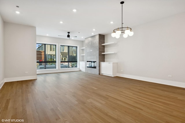 unfurnished living room with ceiling fan with notable chandelier, a premium fireplace, and hardwood / wood-style floors