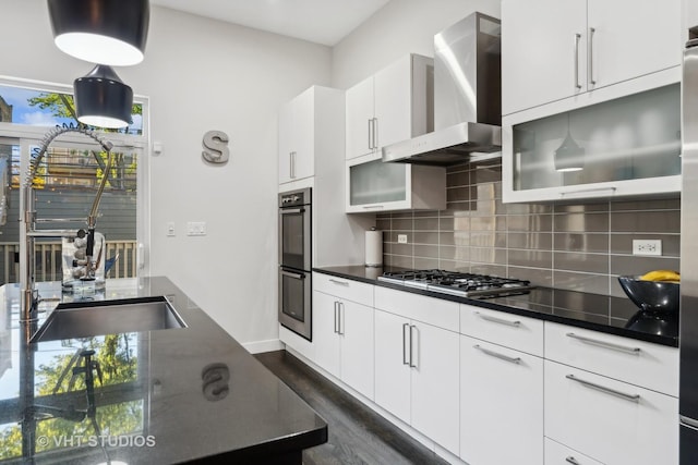 kitchen with stainless steel appliances, decorative backsplash, wall chimney exhaust hood, white cabinets, and sink