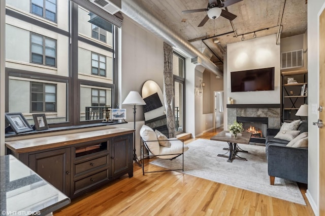 living room featuring a towering ceiling, light wood-type flooring, a stone fireplace, and ceiling fan